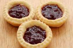 Three miniature blackberry tarts on a wooden surface